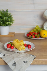 Yellow bright pancakes with fresh strawberries on a white plate stands on the table