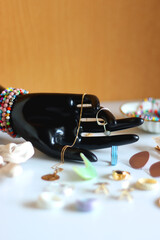Hand figurine, sunglasses, gold jewelry, colorful bead jewelry, statement rings and various hair accessories on the white table. Selective focus.