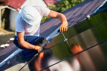 Worker building photovoltaic solar panel system on rooftop of house. Man engineer in helmets and...