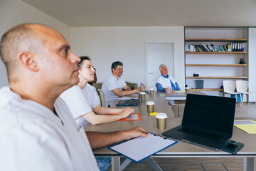 Group of healthcare workers in white uniforms attending a training session with laptops and...