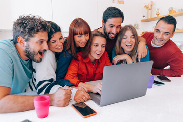 Excited group of friends gathered around a laptop, smiling and sharing a joyful moment at home