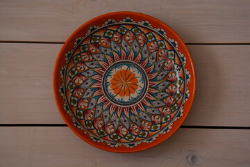 A beautiful round ceramic dish with oriental patterns lies on a table made of white boards. Top view.