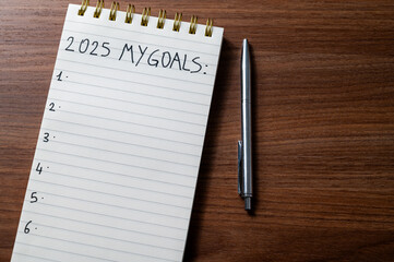 Notepad with text 2025 My Goals, on wooden surface. Priorities and goals for 2025