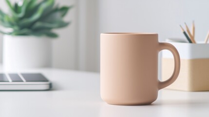 A white mug sits on a table next to a laptop and a potted plant