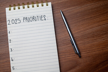 Notepad with text 2025 Priorities, on wooden surface. Priorities and goals for 2025