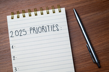 Notepad with text 2025 Priorities, on wooden surface. Priorities and goals for 2025