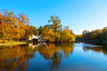 Royal Lazienki Park in Warsaw in fall season. Tranquil lake with gentle ripples, framed by autumn trees and a clear blue sky above