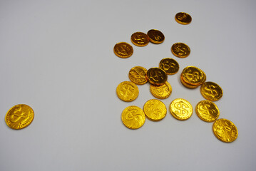 Beautiful, large gold coins, cents with a dollar $ sign are located on a white plastic background. Money candies, a chocolate bar in a gold metal shell.