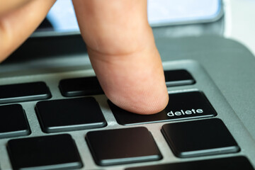 Finger of the computer user, he presses the delete button on the computer keyboard.	