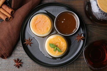 Tasty puddings with caramel sauce served on wooden table, flat lay