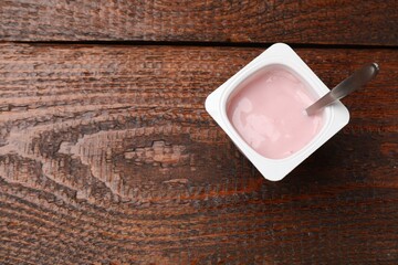Delicious yogurt in plastic cup with spoon on wooden table, top view. Space for text