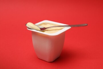 Delicious yogurt in plastic cup with spoon on red background, closeup