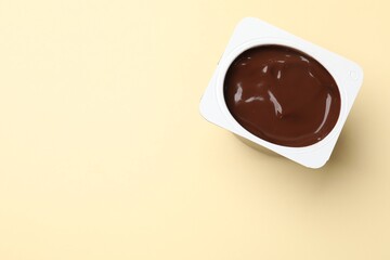 Delicious chocolate yogurt in plastic cup on yellow background, top view. Space for text