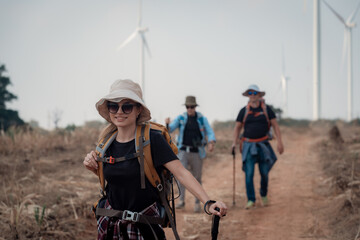 Fototapeta premium Hiker or explorer on journey carrying backpack, trekking poles hiking landscape with wind turbines farm background trekking and trail exploration holiday ecotourism concept.