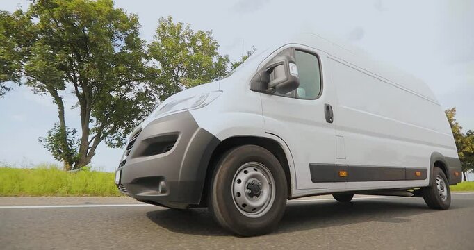 Cargo minibus drives on the highway in sunny weather. White Delivery Van driving along the highway. Fast delivery of goods by minivan.