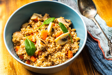 Boiled spelled or spelled porridge with mushrooms, carrots and spinach in a blue bowl on a wooden background with a napkin and spoon. Healthy eating concept. Vegetarian dish.