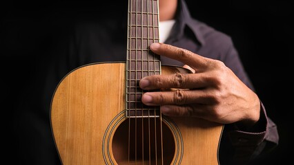 Fototapeta premium The musician's hand gently rests on the guitar's neck, immersing the viewer in a creative atmosphere. The warm light highlights the texture of the wood and creates an intimate ambiance.