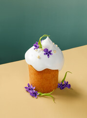 Easter Kulich with White Icing and Violet Flowers on a Green and Yellow Background