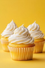 A delightful trio of vanilla cupcakes topped with white icing, placed on a bright yellow background. Perfect for any celebration or indulgence.