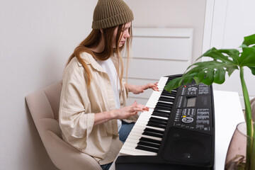 Young woman playing electronic piano at home. A red-haired girl learns to play the synthesiser.