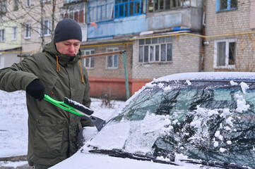 a man cleaning car from snow a brush with an ice scrap