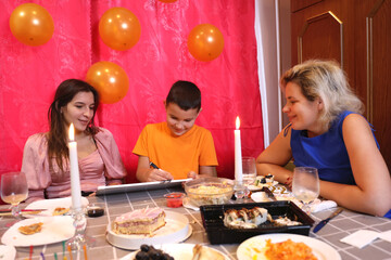 A girl with her family is sitting at the table and celebrating her birthday. Soft lighting.