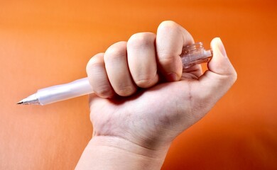 Hand holding and clicking mechanical pencil isolated on horizontal orange brown terracotta colored background.