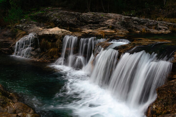 Majestic cascading waterfall over rugged rocks with crystal-clear turquoise water in Loureza, Galicia