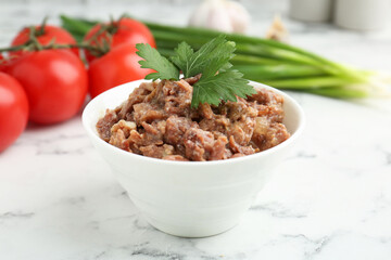 Canned meat in bowl, parsley, tomatoes and green onions on white marble table, closeup