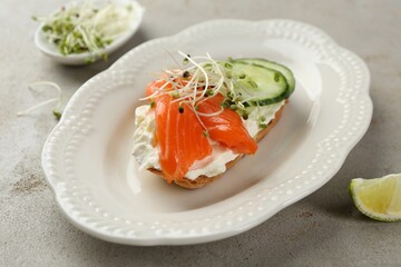 Delicious bruschetta with salmon, cream cheese and cucumber on light table, closeup