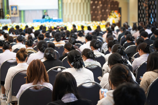 A large group of people seated in rows of chairs, attentively participating in a formal event held in a spacious hall.
