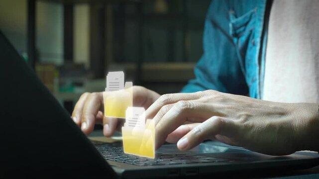 Close-up of hands typing on a laptop with holographic digital documents and a folder icon floating above, representing file management, data organization, and online documentation.