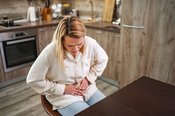 Woman experiences discomfort in modern kitchen setting, seeking relief