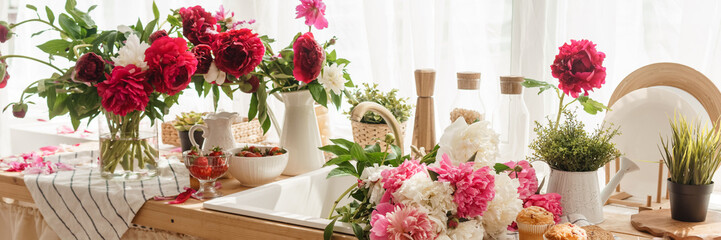 The kitchen countertop is decorated with peonies. The interior is decorated with spring flowers. Pink peonies and sweet cupcakes on a wooden countertop. Interior details.