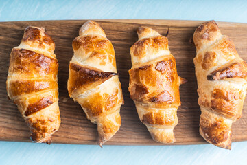 Croissants on a wooden board on a blue background. Copyspace, place for text.