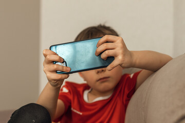 Boy playing video games at home sitting on the couch. Smartphone addiction concept 
