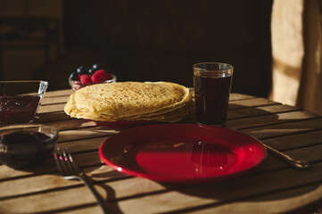 Stack of crepes served with drinks and berries on a wooden table