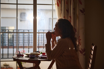 Woman enjoying breakfast near a sunlit window during a tranquil morning