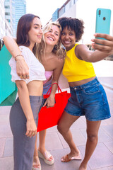 Three young women sitting outdoors, smiling, and taking a playful selfie together. Perfect for concepts like friendship, happiness, social media, and outdoor lifestyle.