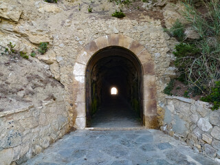 Fototapeta premium A stone tunnel entrance leading to a bright exit on a rocky hillside in a secluded area during daylight