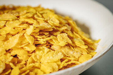 A white bowl filled with golden cornflakes, showcasing their crunchy texture and bright yellow color.