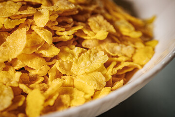 A white bowl filled with golden cornflakes, showcasing their crunchy texture and bright yellow color.