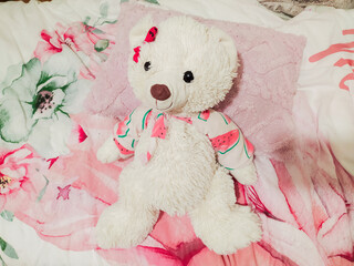 Adorable fluffy white teddy bear in a watermelonprint outfit rests on a pink floral bedspread. Perfect for childrens products, websites, blogs, or illustrating stories about friendship and comfort.