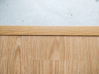 Highresolution image showcasing light wood flooring with a thin wood trim separating it from a light grey concrete background.