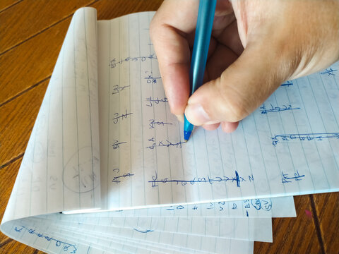 Closeup shot of a hand writing notes in a notebook with a blue pen.  The lined paper shows various calculations and sketches.