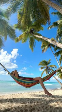 happy woman relaxing on a colorful hammock on a tropical beach with palms and turquoise sea