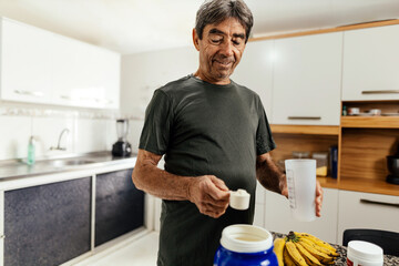 Elderly sportsman preparing protein shake in his kitchen