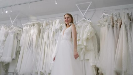 Smiling woman in a stunning white wedding gown, showcasing her elegant style in a bridal shop filled with beautiful dresses, radiating joy and excitement for her big day