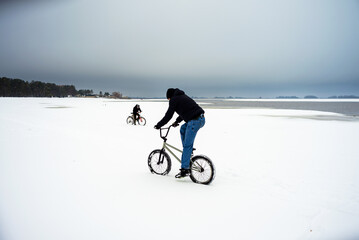 Fototapeta premium Two teenagers ride bicycles in the snow in winter.