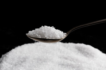 A metal spoon with salt and a pile of salt next to it. Table salt.